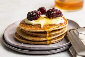 Stack of fluffy protein pancakes topped with Greek yoghurt, berries and honey on a ceramic plate.