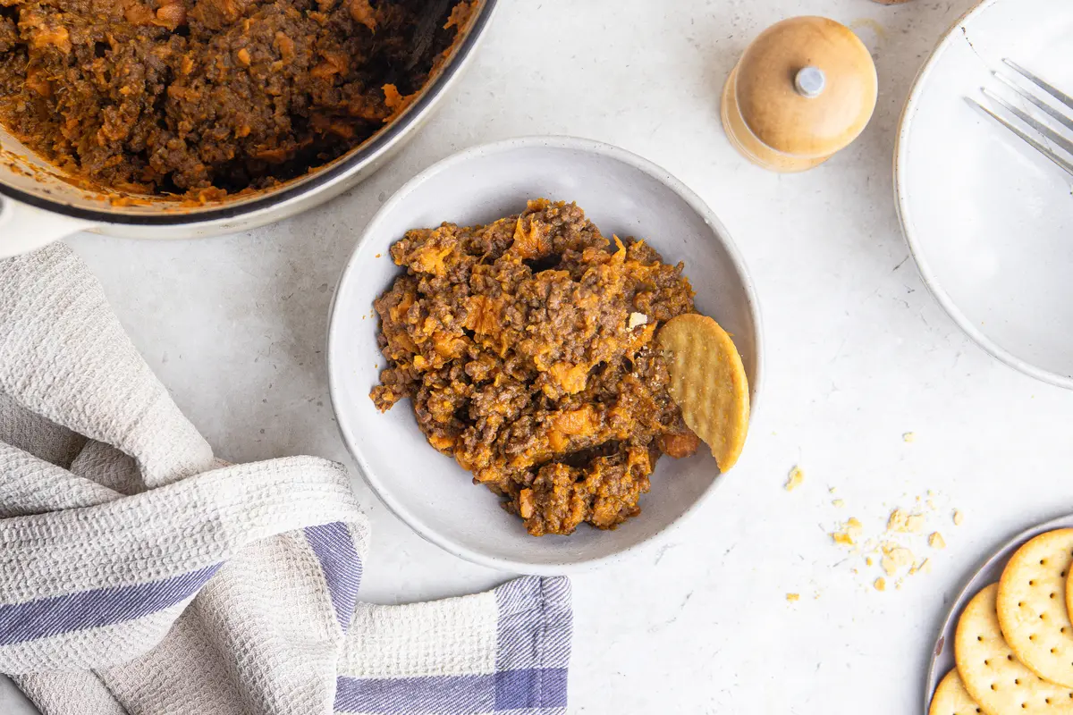 Overhead serving shot of sweet potato stovies in a bowl with crackers, extra portions and the cooking pan nearby.