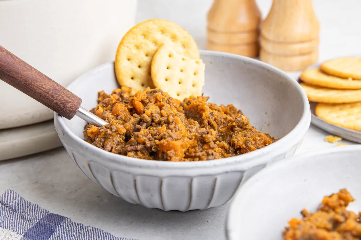 Side-angle shot of sweet potato stovies made with beef mince and chunky sweet potato, served in a grey bowl with crackers on the side.