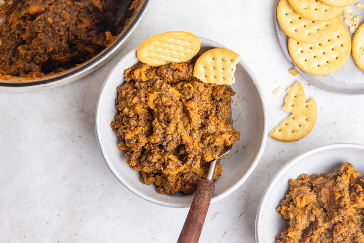 Overhead shot of hearty sweet potato stovies with lean beef mince served in a bowl, with crackers, a fork and the pan in the background.