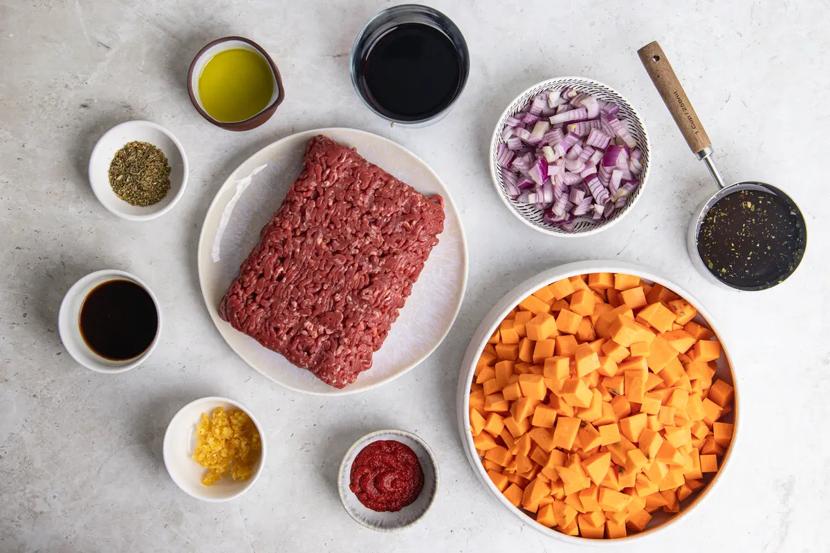 Flat lay of ingredients for sweet potato stovies, including lean beef mince, sweet potato, red onion, stock, tomato purée and seasonings.