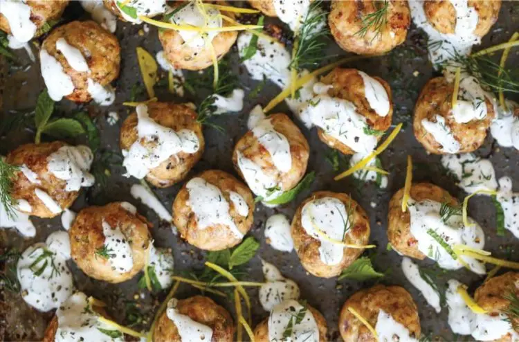A plate of Greek turkey meatballs drizzled with tzatziki and sprinkled with parsley.