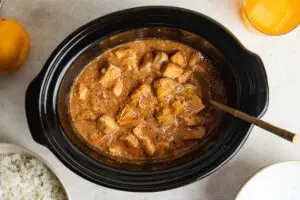 Overhead view of Slow Cooker Irn-Bru Chicken cooked until tender in a thick, glossy orange sauce, finished with fresh orange zest and black pepper.