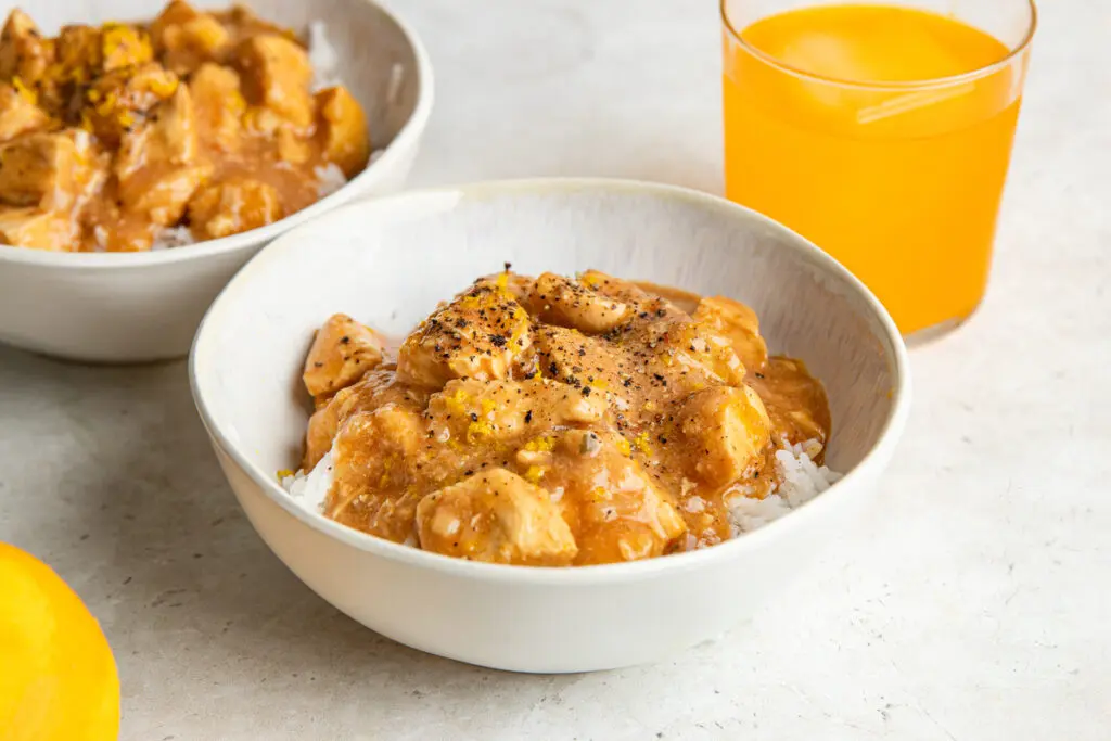 A bowl of Slow Cooker Irn-Bru Chicken served over fluffy white rice, with tender chicken breast coated in the rich orange sauce and finished with orange zest.