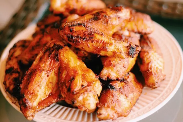 Grilled chicken wings with crispy skin and a dry bbq marinade rub, served on a platter with dipping sauces.