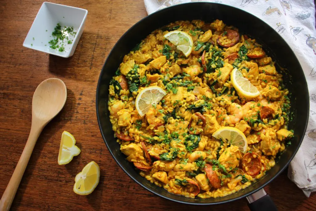 A vibrant plate of golden chicken and chorizo paella, packed with juicy prawns, tender chicken, and smoky chorizo, garnished with fresh spinach and a squeeze of lemon.