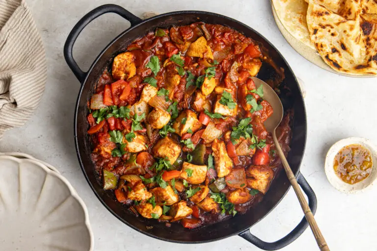 Chicken dopiaza in a black pan with peppers, onions, coriander and naan bread.