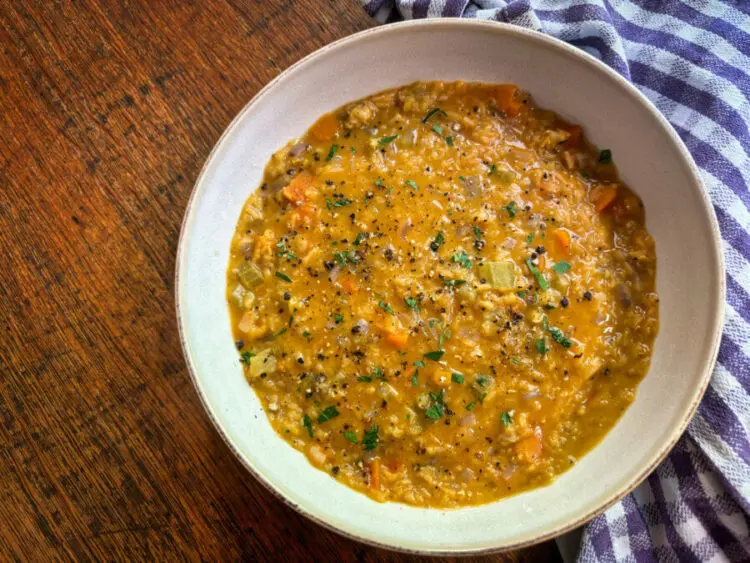 Bowl of hearty red lentil high protein soup with carrots, celery, and fresh herbs