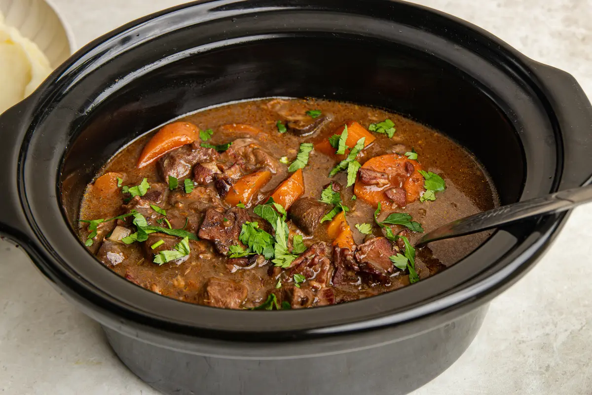 Rich slow cooker beef bourguignon ready to serve, with tender chunks of beef, smoky bacon, carrots and mushrooms in a glossy red wine sauce, finished with fresh parsley.