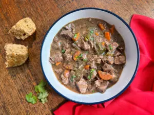 A steaming bowl of slow-cooked Italian Beef Stew, garnished with fresh herbs, with a slice of crusty bread on the side.