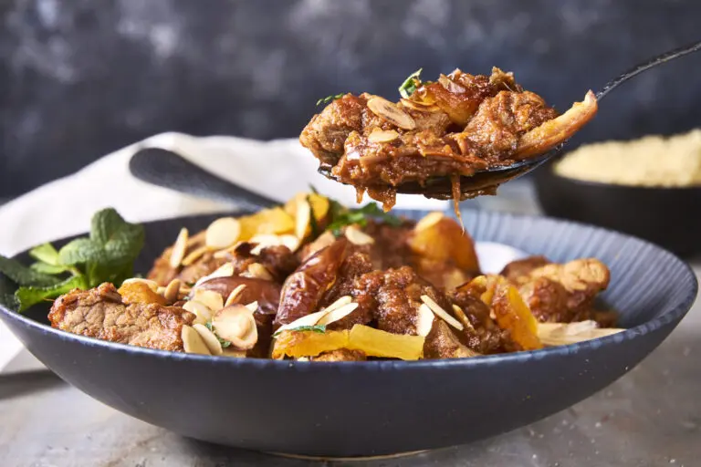 Spoonful of Moroccan lamb tagine lifted from a serving dish with almonds