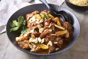 Moroccan lamb tagine in a black bowl topped with almonds, apricots and fresh mint.
