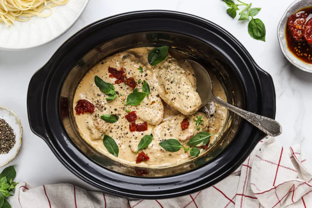 Slow cooker filled with creamy Marry Me Chicken topped with basil and sundried tomatoes.