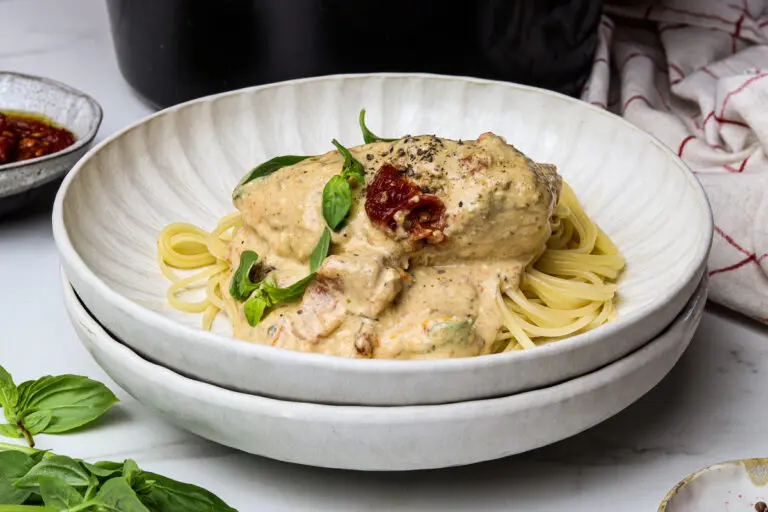 Flat lay of Marry Me Chicken on spaghetti with basil beside the slow cooker.