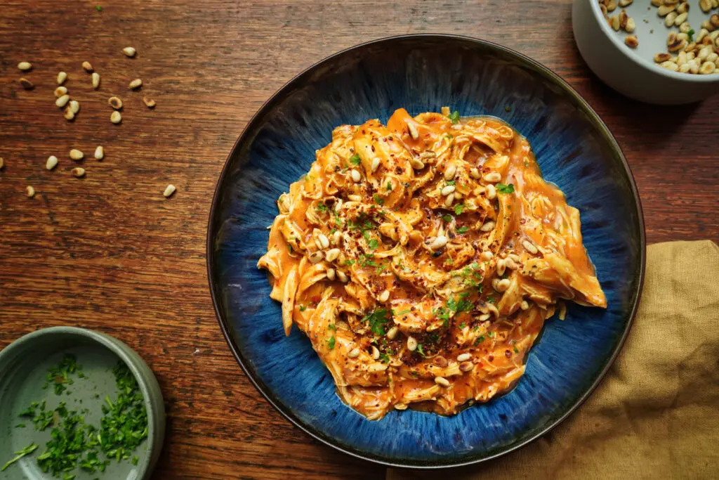 A bowl of slow-cooked harissa chicken, garnished with fresh herbs, served in a rich, red sauce.