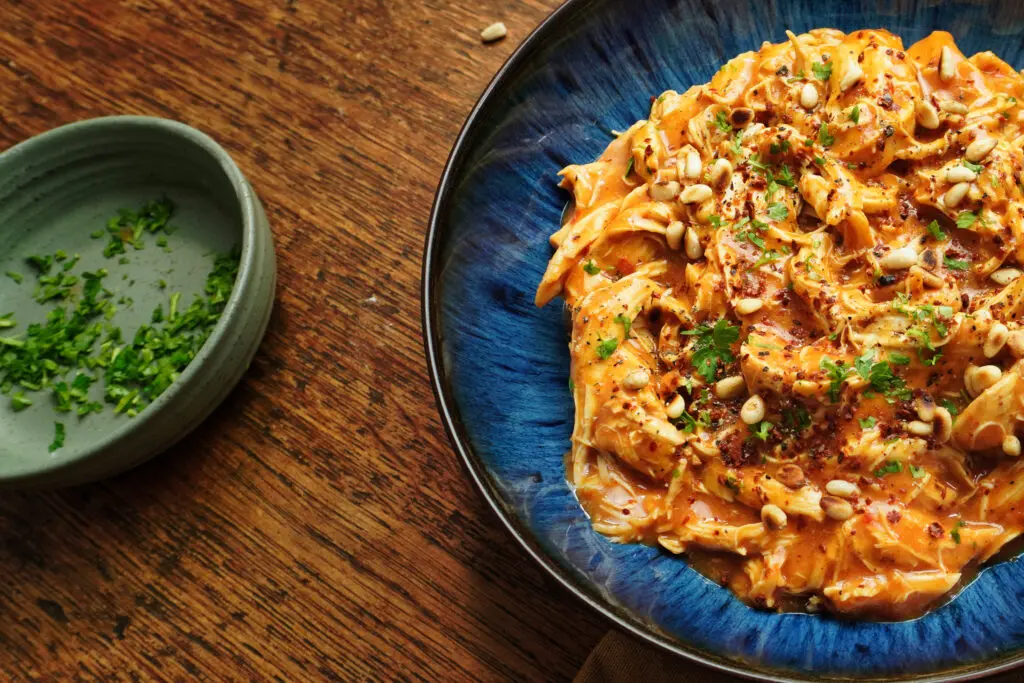 A bowl garnished with fresh herbs, with its rich, red sauce glistening. The tender chicken is shredded and coated in the spicy, smoky sauce, ready to be served with rice or couscous.