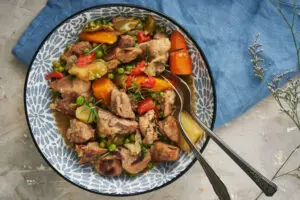 Flat lay of a bowl of slow-cooked Caldereta de Cordero, filled with tender lamb, potatoes, carrots, peppers, and peas, garnished with fresh rosemary.