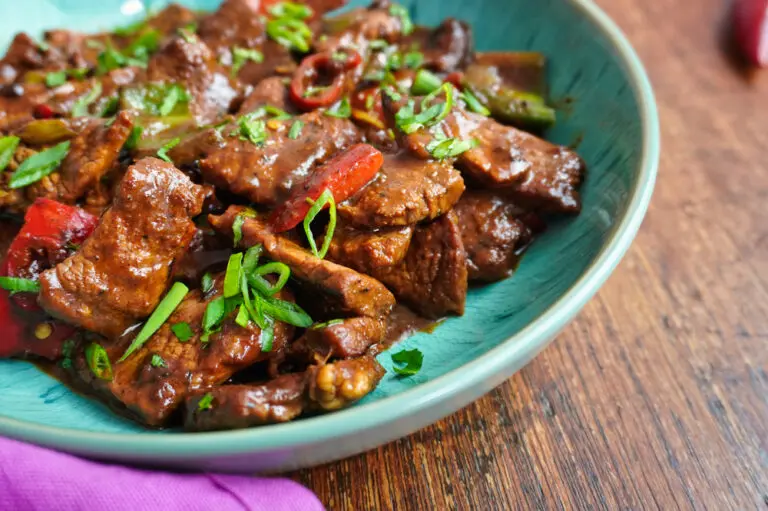 Side angle of Jamaican pepper steak in a bowl, highlighting the thick sauce clinging to the beef and peppers, with green onion garnish.