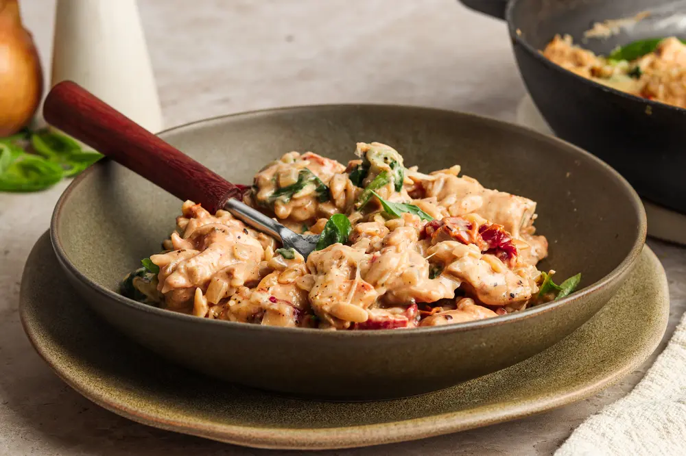 Bowl of creamy marry me chicken orzo with sun-dried tomatoes and basil.