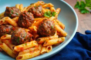 A close-up shot of tender, air-fried meatballs covered in a vibrant tomato sauce, nestled among penne pasta. The fresh parsley garnish adds a pop of colour to the dish.