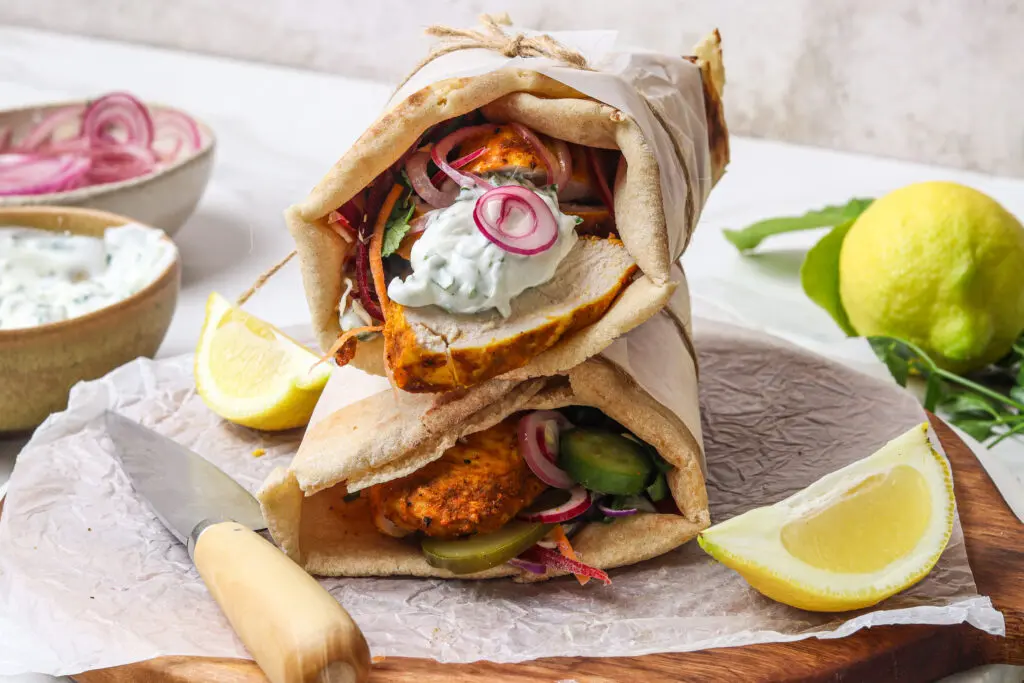 Close-up of stacked Air Fryer Chicken Shawarma Wraps, showcasing the juicy, spiced chicken, crisp vegetables, and creamy yoghurt sauce spilling from the flatbread. Pickled onions and cucumbers peek through the layers.