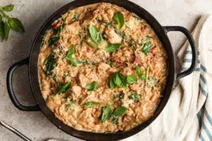 Creamy marry me chicken orzo in a black skillet topped with basil and cheese.