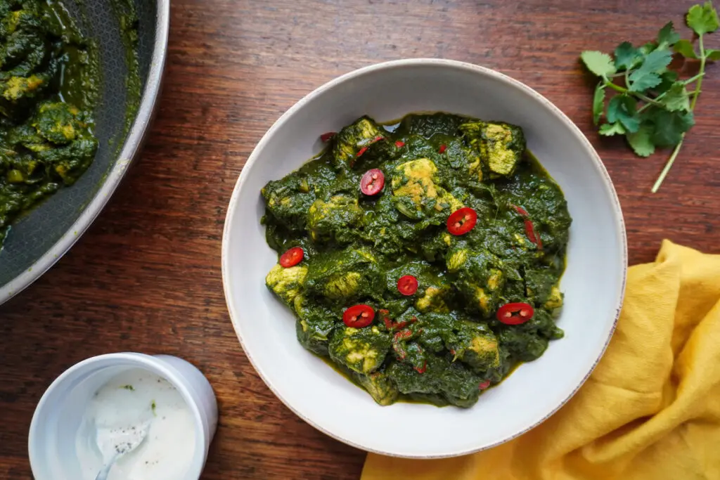 Bowl of Palak Chicken Curry in rich green sauce, garnished with red chilli slices, on rustic wooden surface