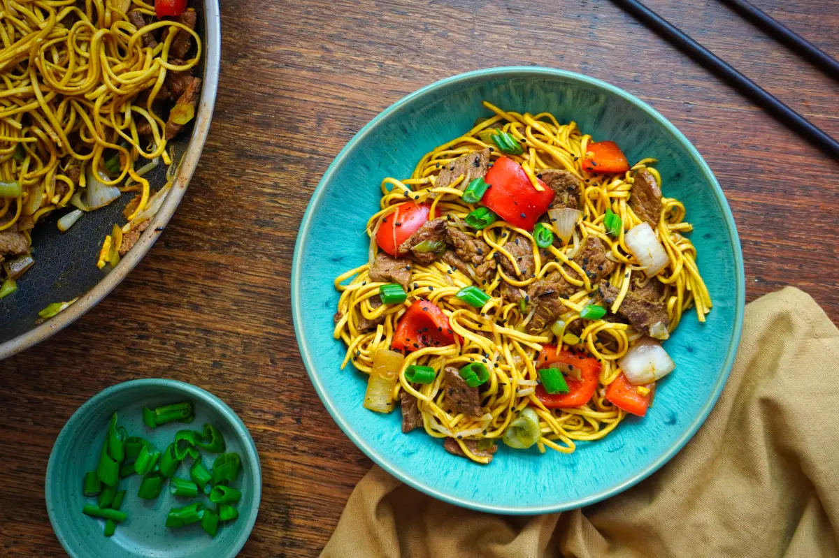 Wok-fried Beef Chow Mein served in a blue bowl with chopsticks.