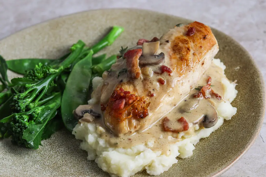 Creamy chicken supreme with bacon slices and mushrooms, served hot on a plate.