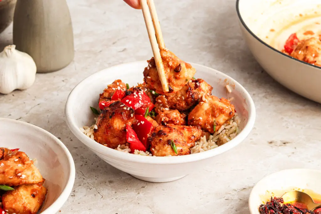 Manchurian Chicken served in bowl over rice with chopsticks lifting a chicken piece