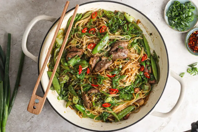 Overhead shot of a large white pan filled with noodles, duck and colourful garnishes