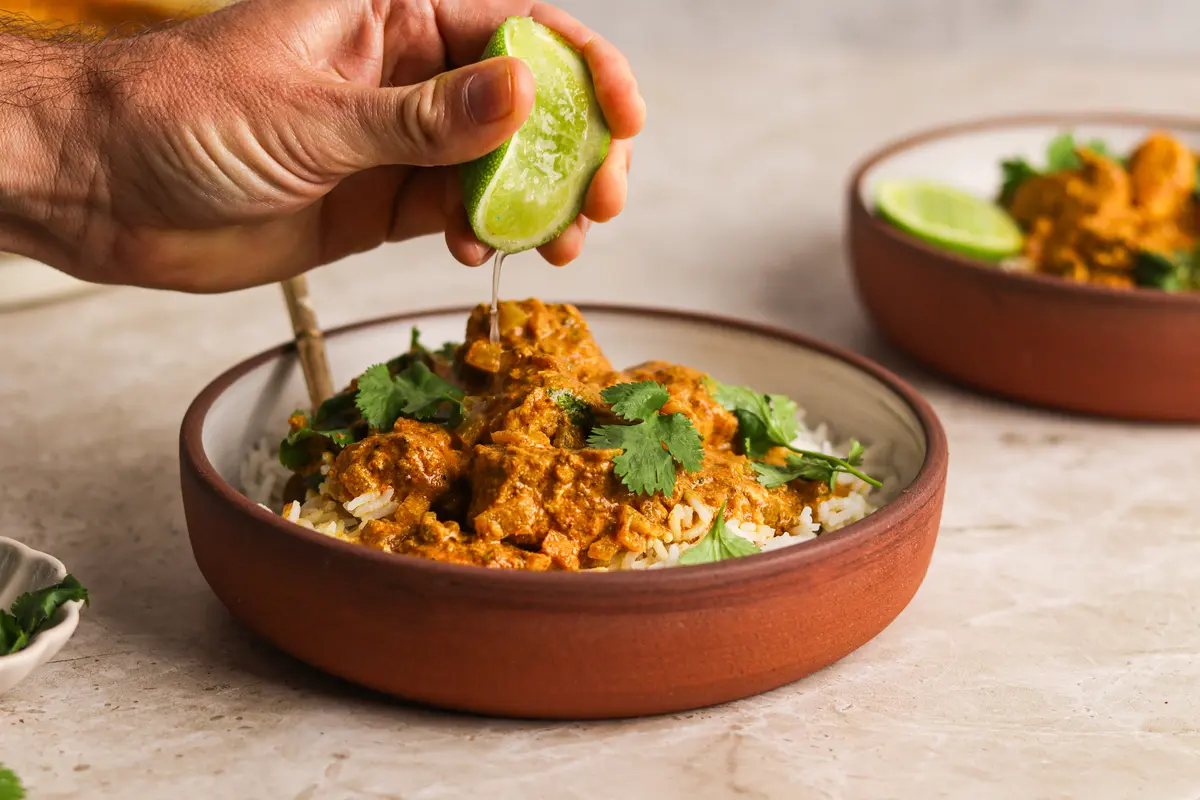 Hand squeezing fresh lime over creamy Sri Lankan chicken curry with coriander and rice