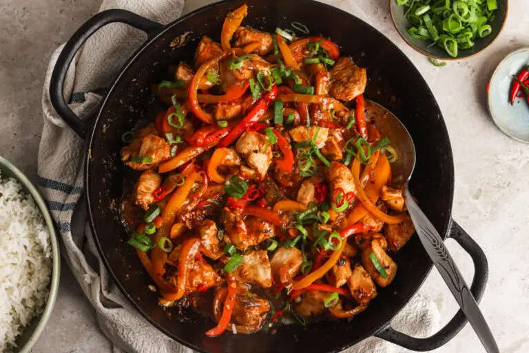 Honey chilli chicken stir-fry in black pan with sliced peppers and spring onions
