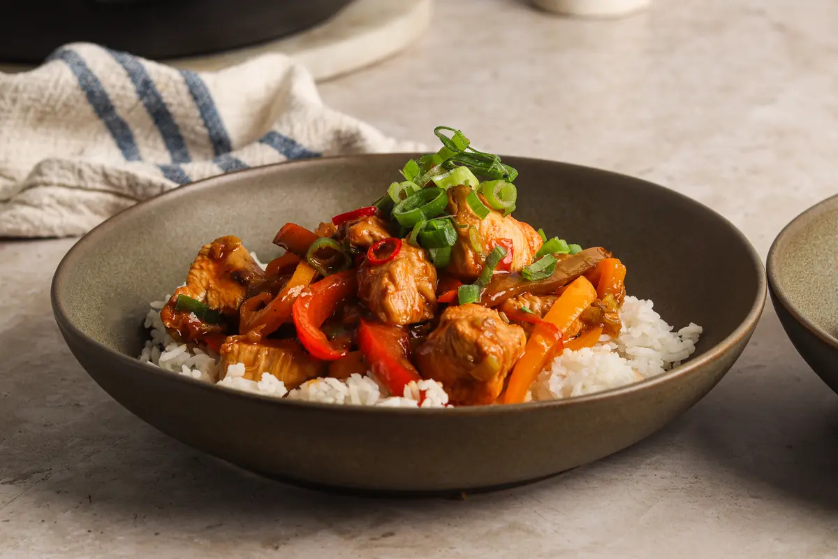 Bowl of honey chilli chicken served over white rice and topped with fresh spring onions