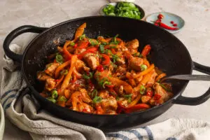 Close-up of honey chilli chicken in wok with colourful peppers and spring onions