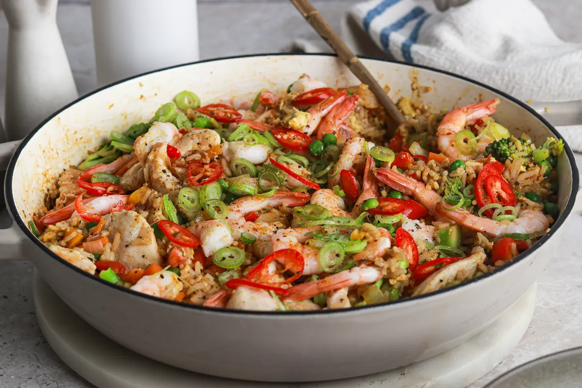Singapore Fried Rice in a white casserole dish with prawns, peppers, and spring onions.