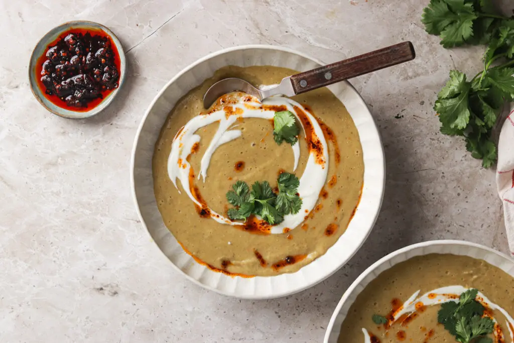 Creamy Sri Lankan lentil soup with coconut swirl, chilli oil, and coriander garnish in white bowl.