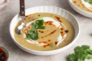 Bowl of Sri Lankan lentil soup with yoghurt drizzle, coriander, and chilli oil, spoon inside.