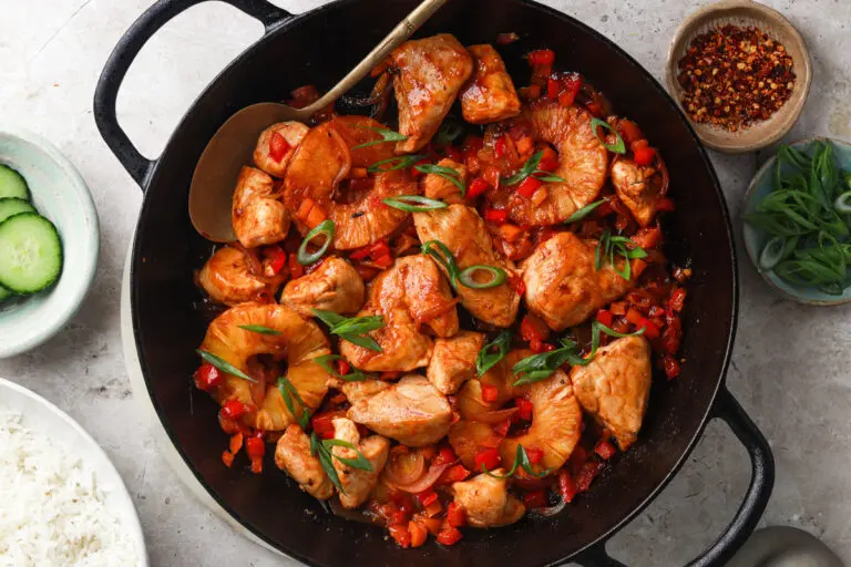 Hawaiian Chicken cooked in a black pan with pineapple rings, peppers and spring onions.