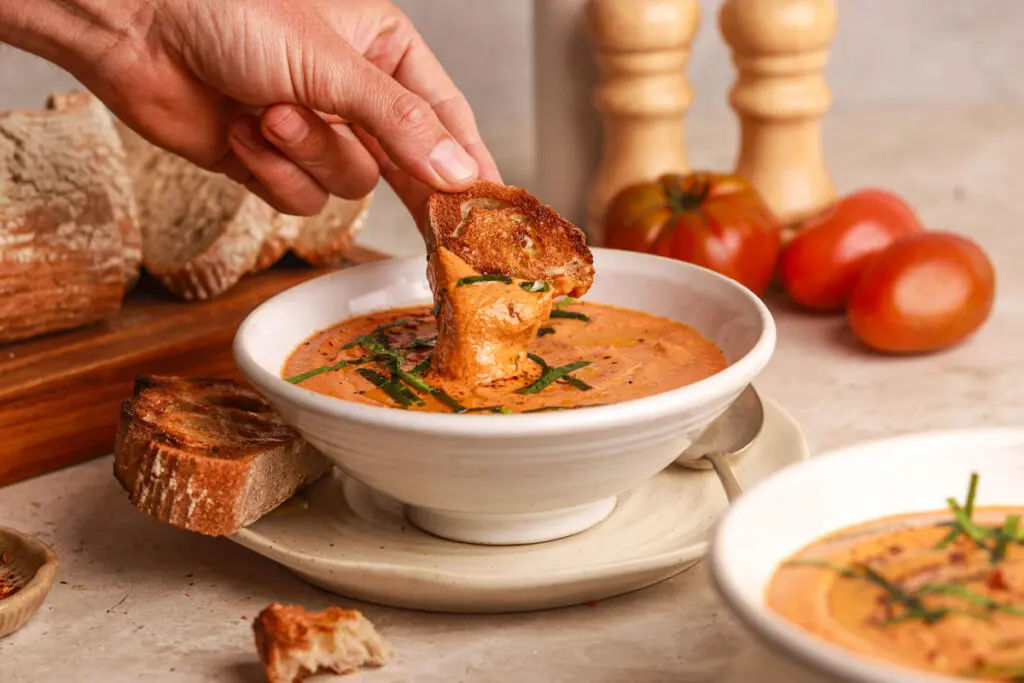 Dipping crusty bread into creamy high protein tomato soup with roasted tomato flavour