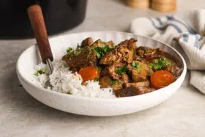 Bowl of Slow Cooker Beef Casserole served with fluffy white rice and parsley garnish.