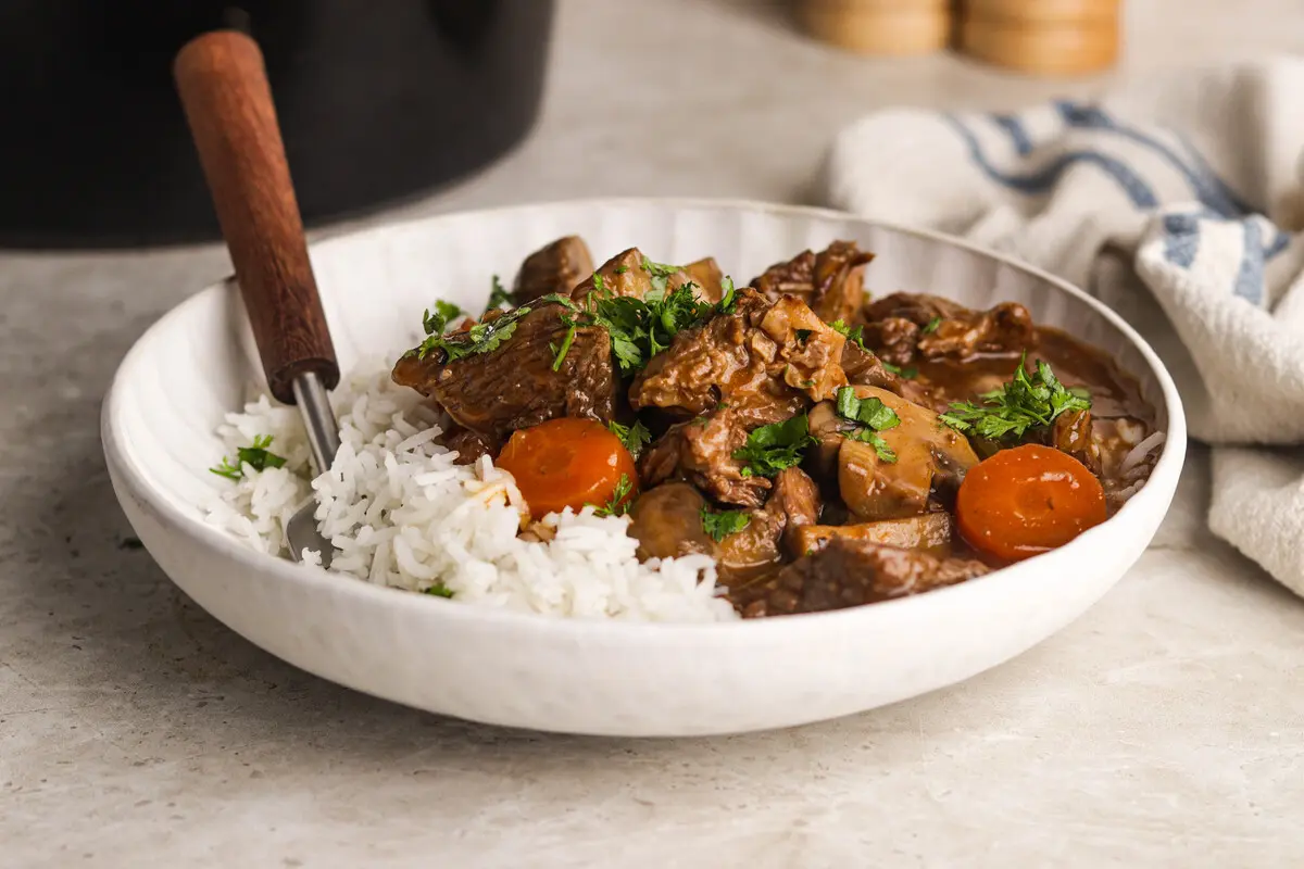 Bowl of Slow Cooker Beef Casserole served with fluffy white rice and parsley garnish.