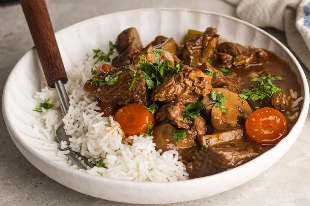 Plate of Slow Cooker Beef Casserole with rice, mushrooms, carrots, and fresh parsley.