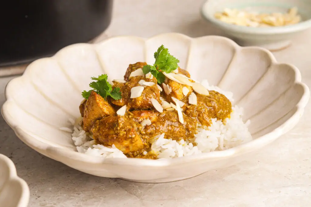 Bowl of creamy slow cooker chicken korma served over basmati rice with almonds