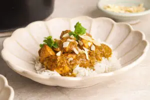 Bowl of creamy slow cooker chicken korma served over basmati rice with almonds