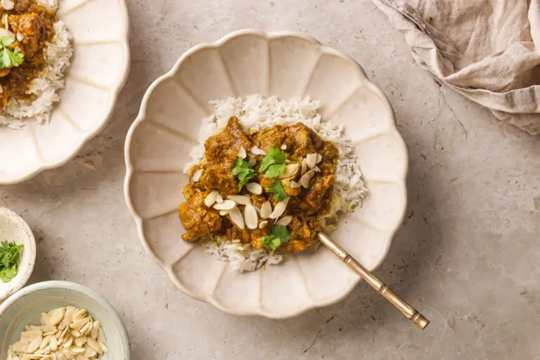 Flat lay of plated chicken korma with rice, flaked almonds, and coriander garnish.