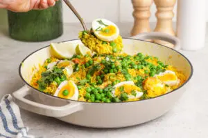 Spoon lifting a serving of kedgeree with egg, peas and yellow curried rice.