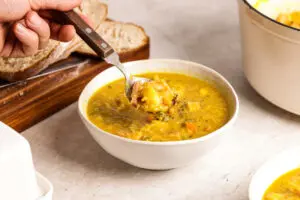 Spoon lifting thick Scottish lentil soup with ham hock, lentils and vegetables