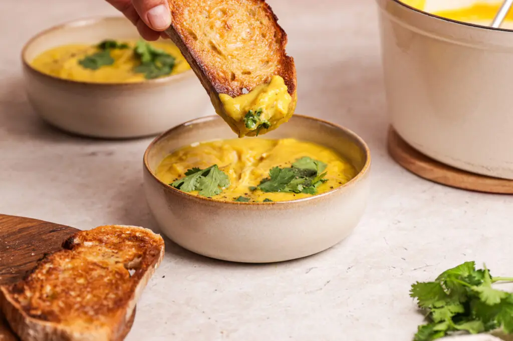 Curried parsnip soup with coriander as toasted bread is dipped into a creamy golden bowl