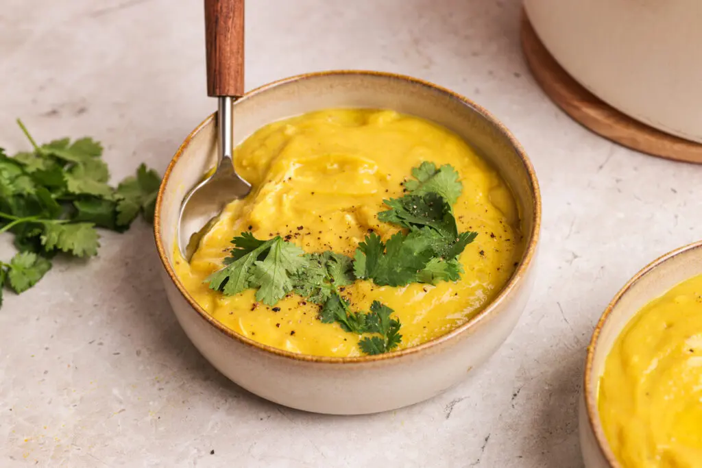 Thick curried parsnip soup with coriander leaves and spoon in a ceramic bowl